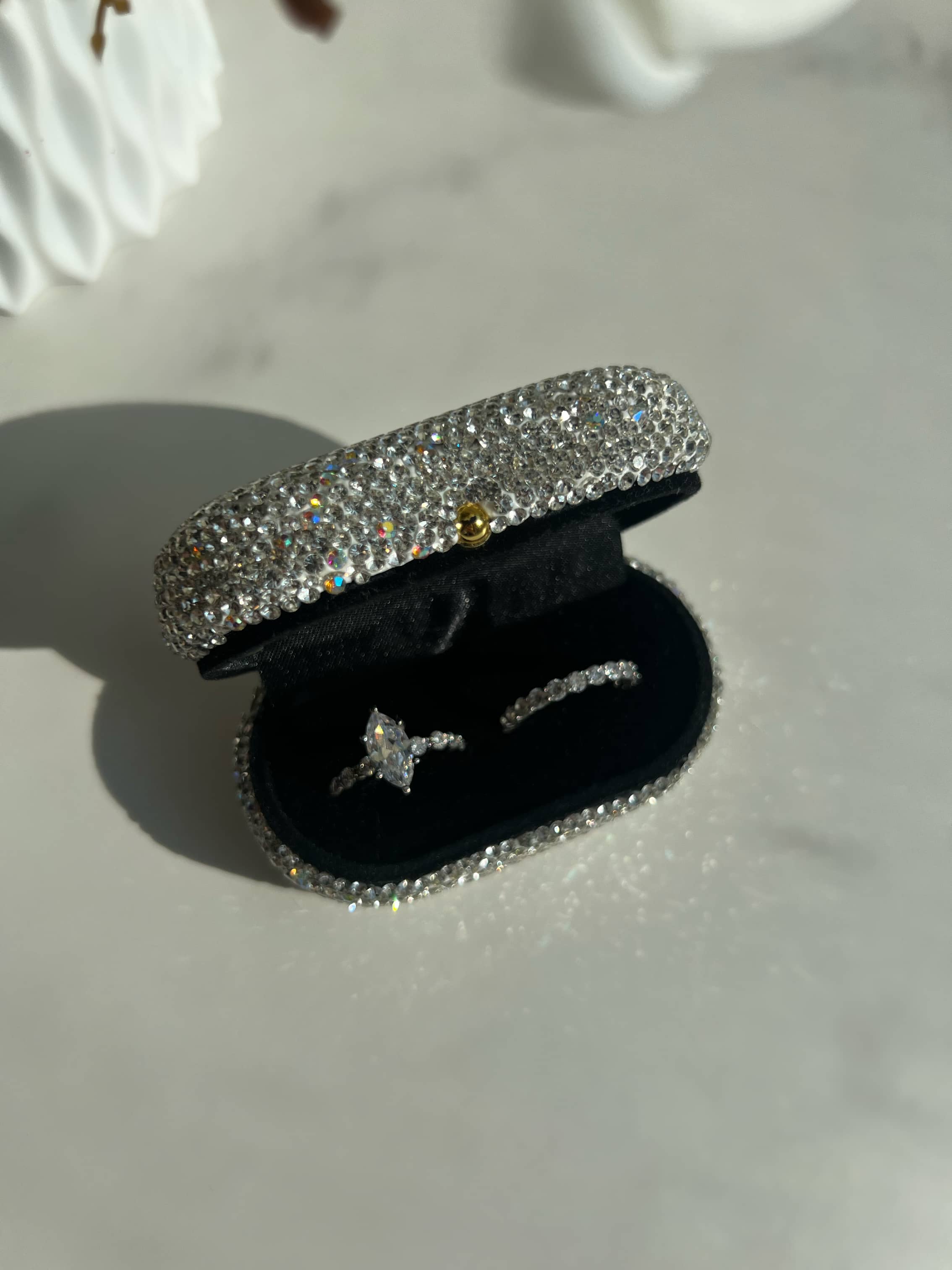 A stunning silver marquise-shaped center stone diamond ring, surrounded by smaller circle diamonds on both sides, along with a silver round cut eternity band. The ring is displayed in an elegant oval box adorned with clear stones, adding to its sparkle