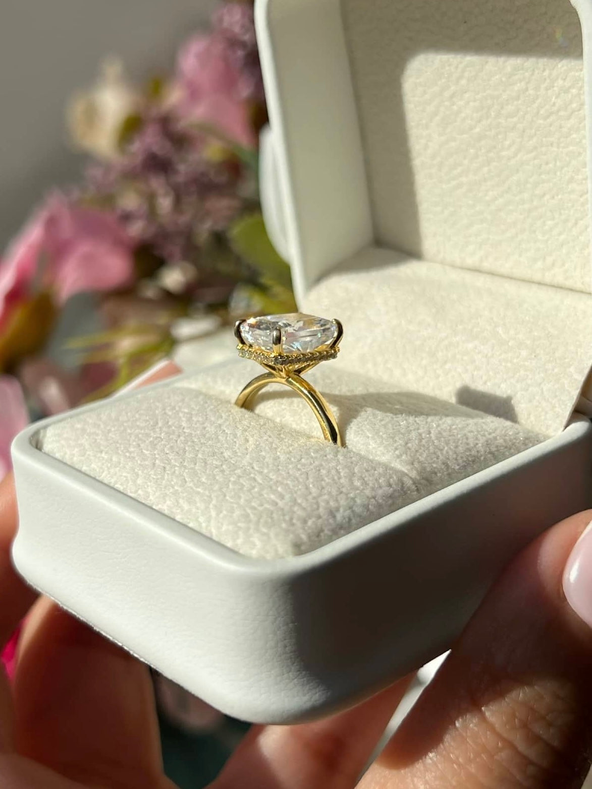 A large radiant-shaped gold diamond sitting in a white square box. The diamond is surrounded by a halo of smaller diamonds, and the band is thin, enhancing the ring’s overall delicate and luxurious appearance. Perfect for special occasions