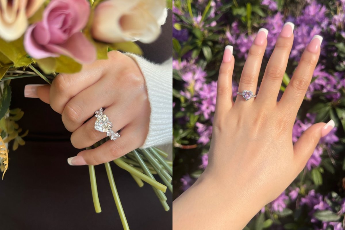 A close-up of two hands showcasing beautiful diamond rings. The left hand features a large, silver heart-shaped diamond ring with smaller diamonds surrounding it. The right hand displays a delicate heart-shaped diamond ring with a pink stone at its centre