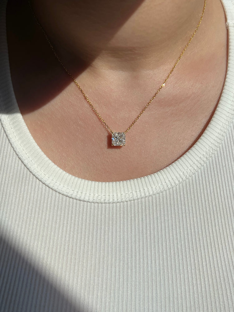 A woman wearing a white ribbed tank top complemented by a chic gold chain necklace featuring a square-shaped diamond pendant, adding a touch of elegance, luxury and sparkle to her everyday look